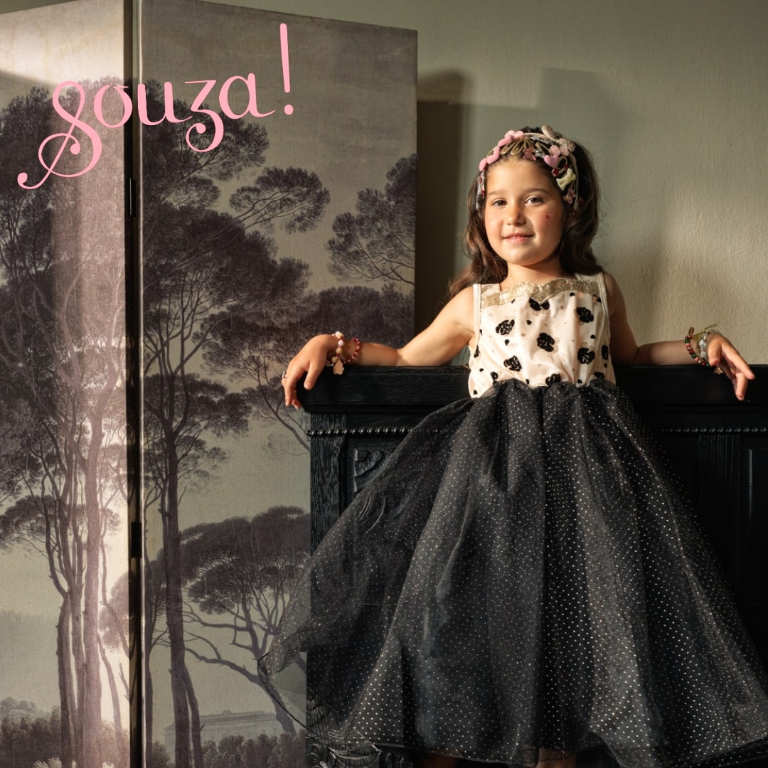 Kind trägt Souza Noella Kostümkleid neben Wandpaneel mit Waldmotiv und rosafarbenem Schriftzug