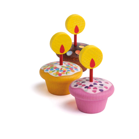 Drei Erzi Holz-Muffins in Gelb, Rosa und Braun mit bunten Streuseln, Kerzen und Flammen