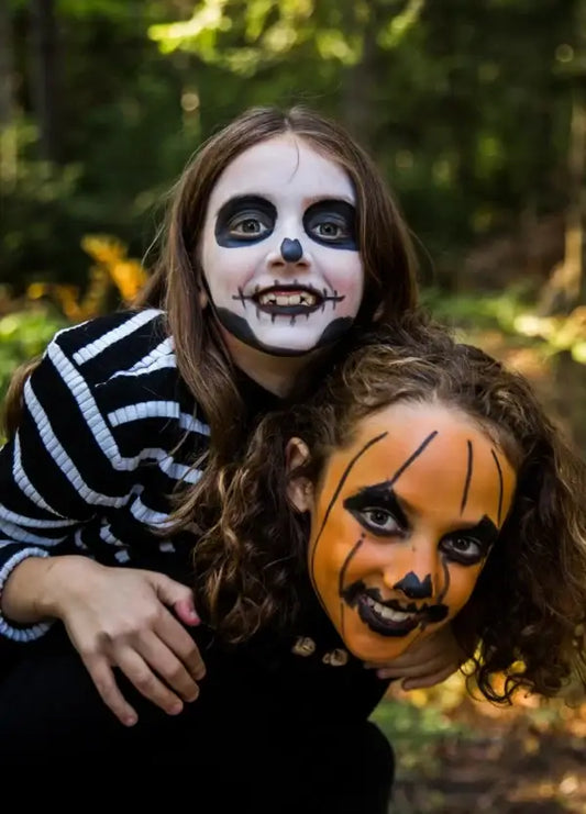 Zwei Kinder mit Halloween-Schmink von Namaki: eine im Skelett-Look, eine mit Kürbis-Design