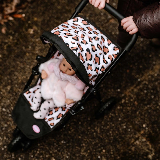 Kind schiebt den Götz 3-Rad Puppen-Buggy mit Leoparden-Muster, darin eine Puppe in weißem Outfit