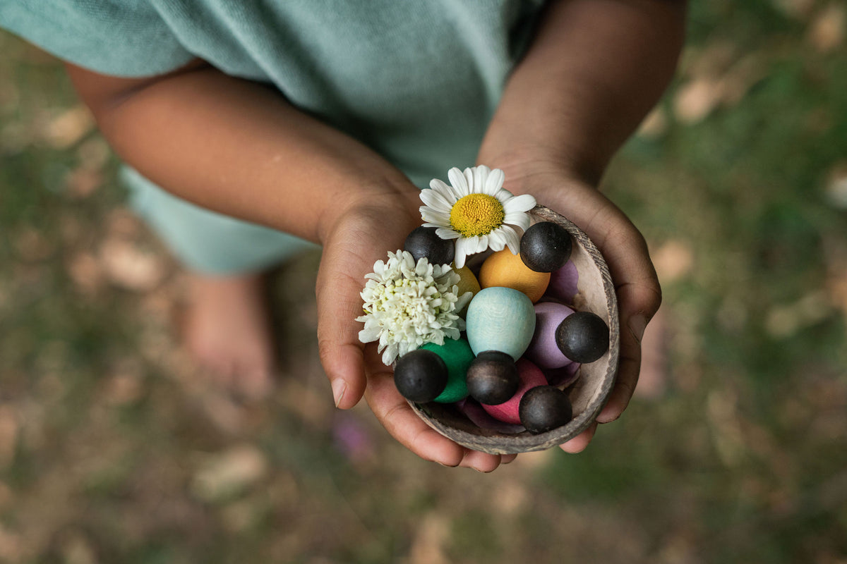 Kinderhände halten die Kokosnussschale mit den Grapat Dark Baby Nins und Blüten