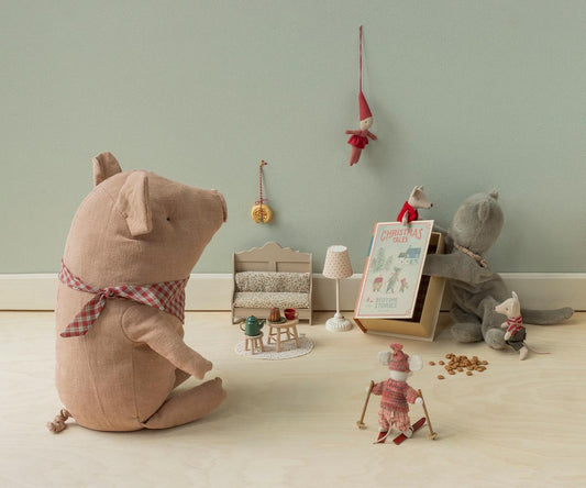 Maileg Buch Christmas Tales lehnt an einem Stoffwolf, davor Mäuse, Puppenmöbel und ein großes Stoffschwein