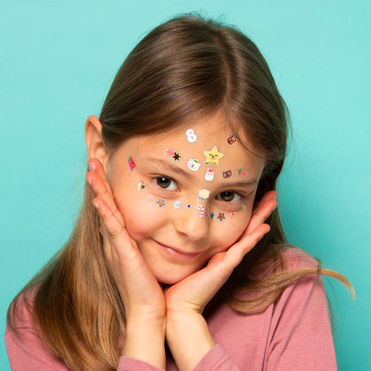 Kind trägt bunte OMY Magic Tree Gesichtssticker mit Sternen und Motiven auf Stirn und Wangen gegen türkisblauem Hintergrund