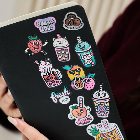 OMY Bubble Tea Sticker auf schwarzer Fläche mit bunten Getränk- und Fruchtmotiven, in Hand gehalten