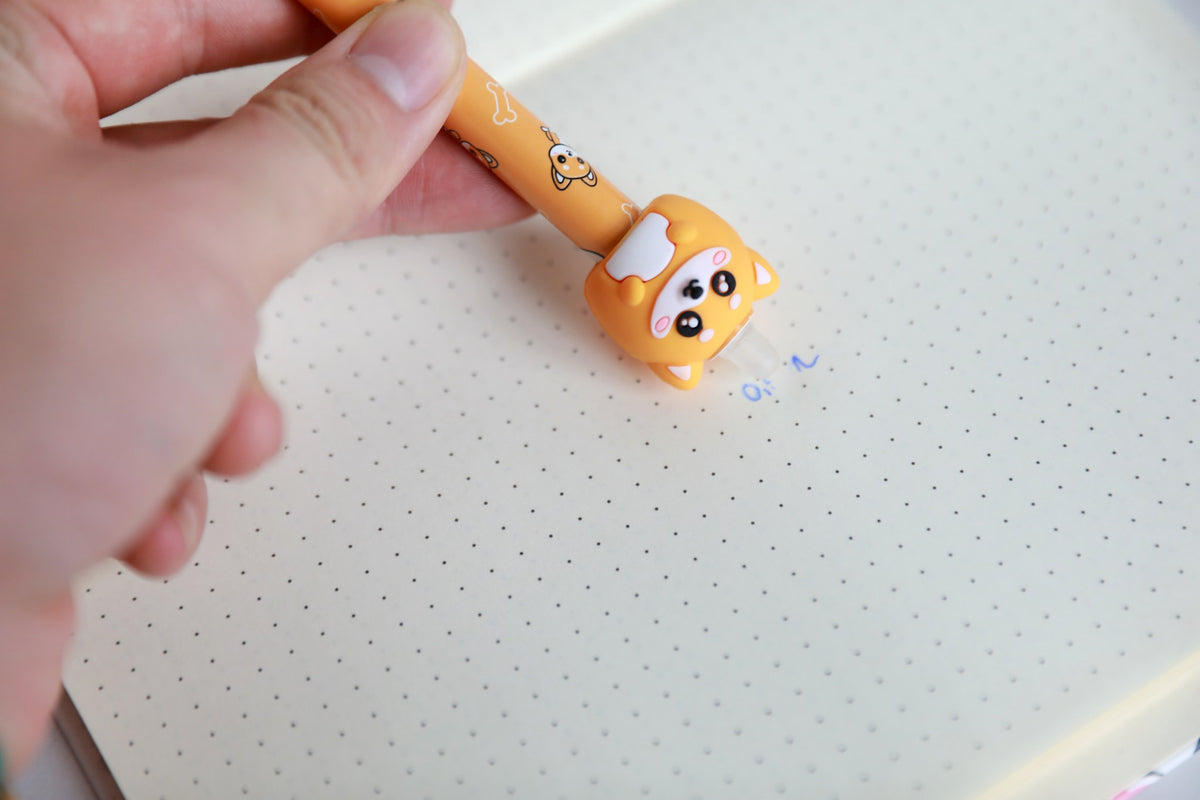 Hand hält den Stift mit Figur Shiba-Hund und radiert damit Schrift auf Punktrasterpapier