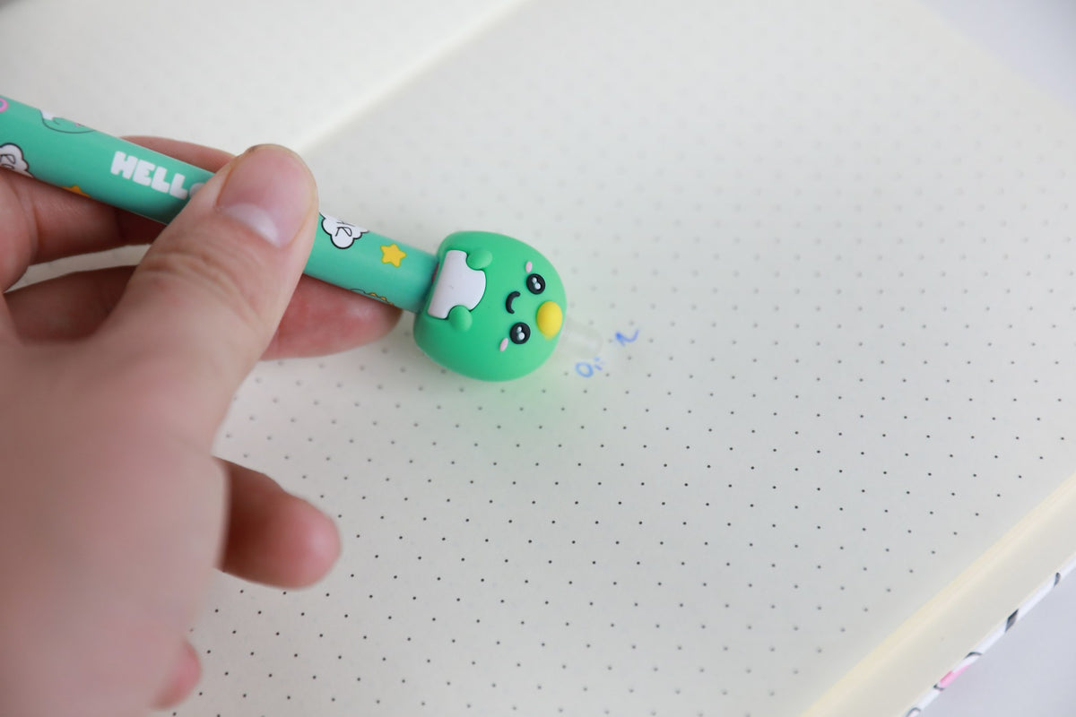 Hand hält den Stift mit Figur Dino und radiert damit Schrift auf Punktrasterpapier