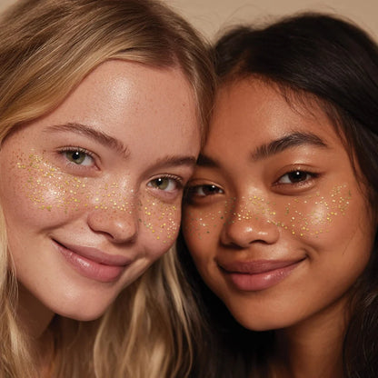 Zwei Mädchen mit goldglitzernden Sommersprossen-Tattoos unter den Augen, lächelnd nah beieinander