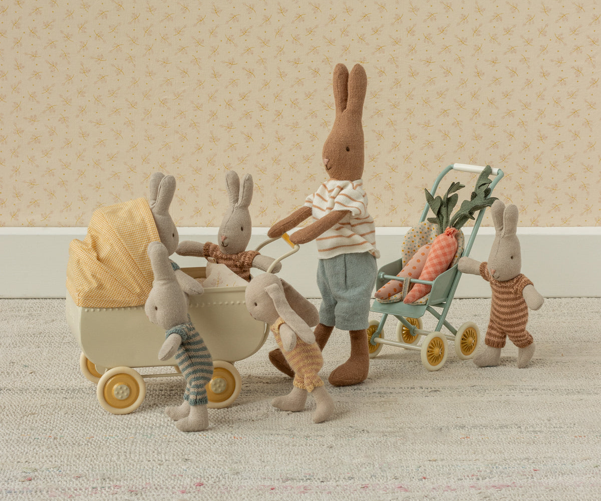 Hasenfamilie aus Stoff schiebt den Maileg Kinderwagen Mikro mit gelbem Verdeck, daneben ein grüner Buggy