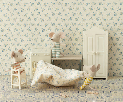 Babymaus sitzt im cremeweißen Maileg Hochstuhl, daneben Mäuse mit Bettwäsche vor Waschmaschine und Schrank