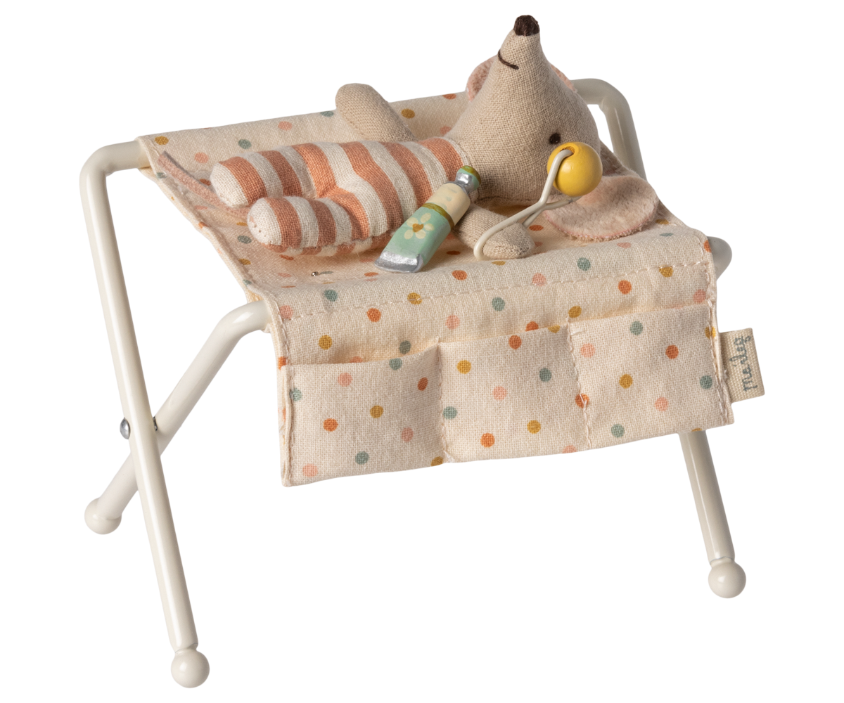 Babymaus liegt auf dem Maileg Wickeltisch mit gestreiftem Kissen, in den Taschen Lotion und Rassel
