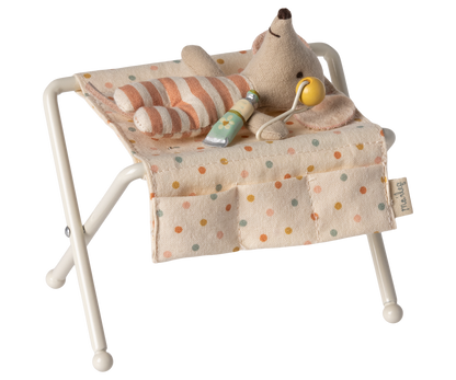 Babymaus liegt auf dem Maileg Wickeltisch mit gestreiftem Kissen, in den Taschen Lotion und Rassel