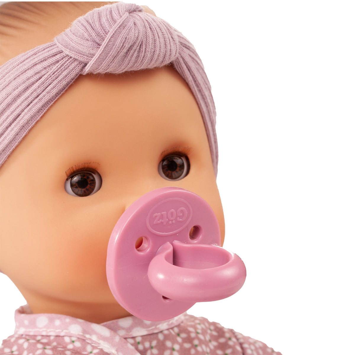 Götz Sleepy Aquini Girl Babypuppe mit lila Stirnband und rosa Schnuller im Mund, Nahaufnahme Kopf und Oberkörper