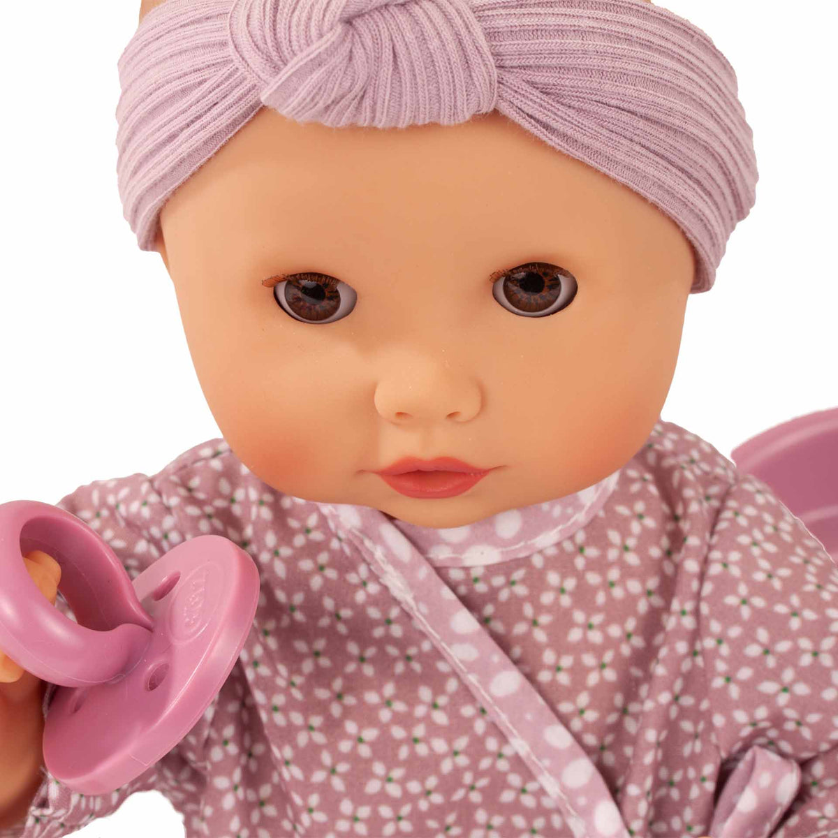 Götz Sleepy Aquini Girl Soft Mood mit lila Stirnband und altrosa Overall, hält einen rosa Schnuller