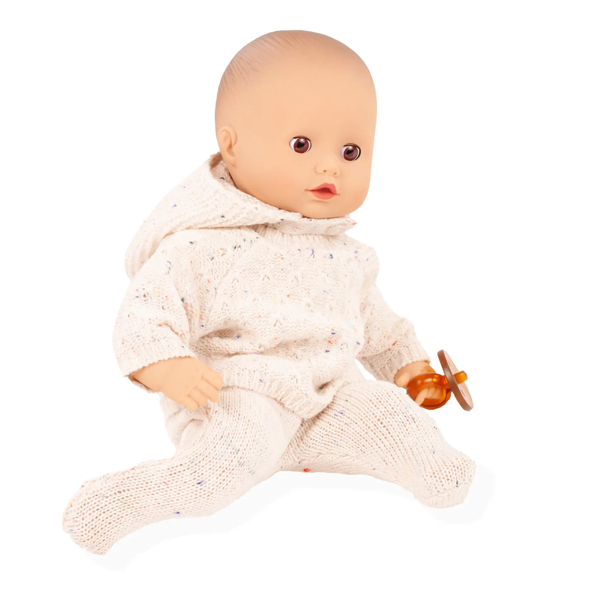 Götz Muffin Baby Alles Strick sitzt im beigen Strickanzug mit Mütze und hält einen orangefarbenen Schnuller in der Hand