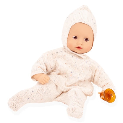 Götz Muffin Baby Alles Strick im beigen Strickanzug mit Mütze, sitzend, daneben ein orangefarbener Schnuller