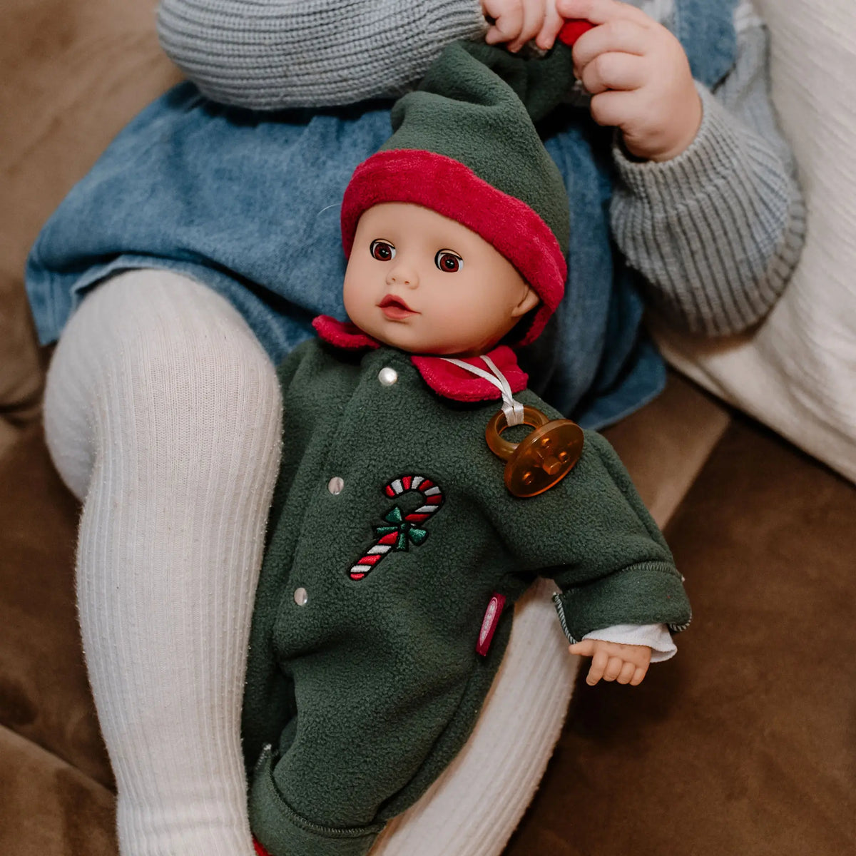 Kind hält die Götz Muffin Baby Christmas Candy im grünen Overall mit Zipfelmütze auf dem Schoß