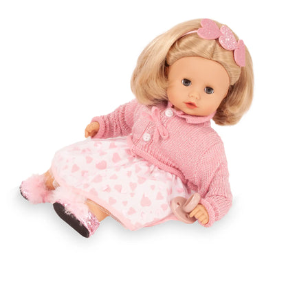 Götz Muffin Puppe sitzt in Seitenansicht, rosa Strickjacke über rosa Kleid mit weißen Herzchen