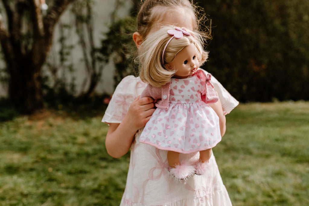 Mädchen hält Götz Muffin Puppe mit blondem Haar und rosa Herzchen-Kleid im Freien, Spielszene
