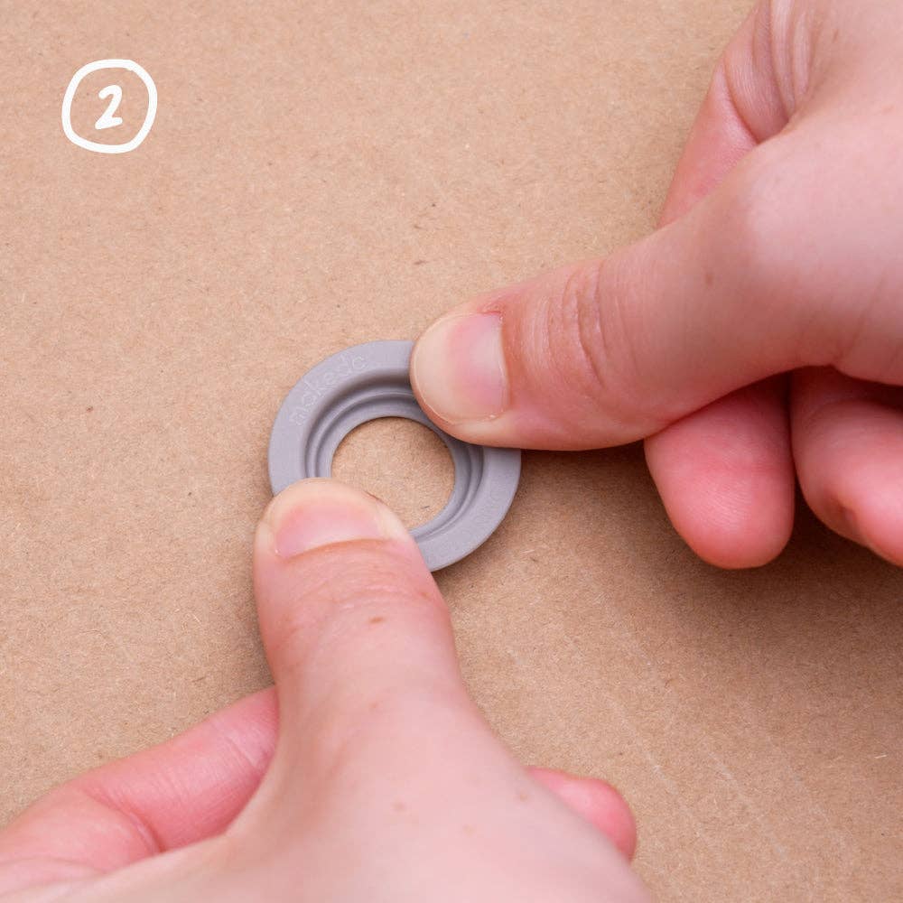 Kinderhände führen einen grauen Makedo Roto-Ring in eine Kartonstruktur ein