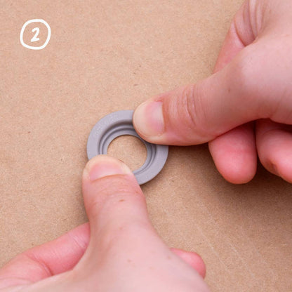 Kinderhände führen einen grauen Makedo Roto-Ring in eine Kartonstruktur ein