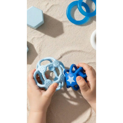 Kinderhände halten den hellblauen und den dunkelblauen Sensorikball über Sand