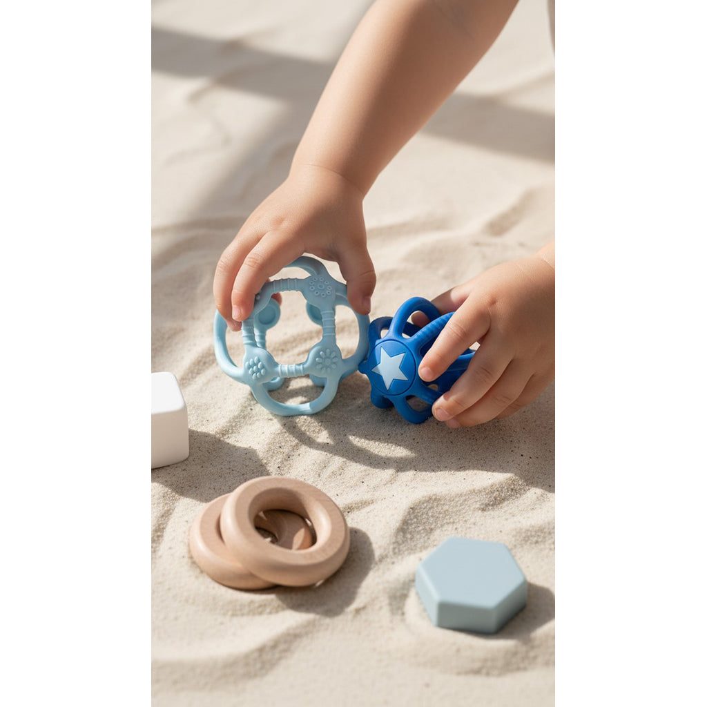 Kind spielt im Sand mit beiden blauen Sensorikbällen, daneben beige Silikonringe
