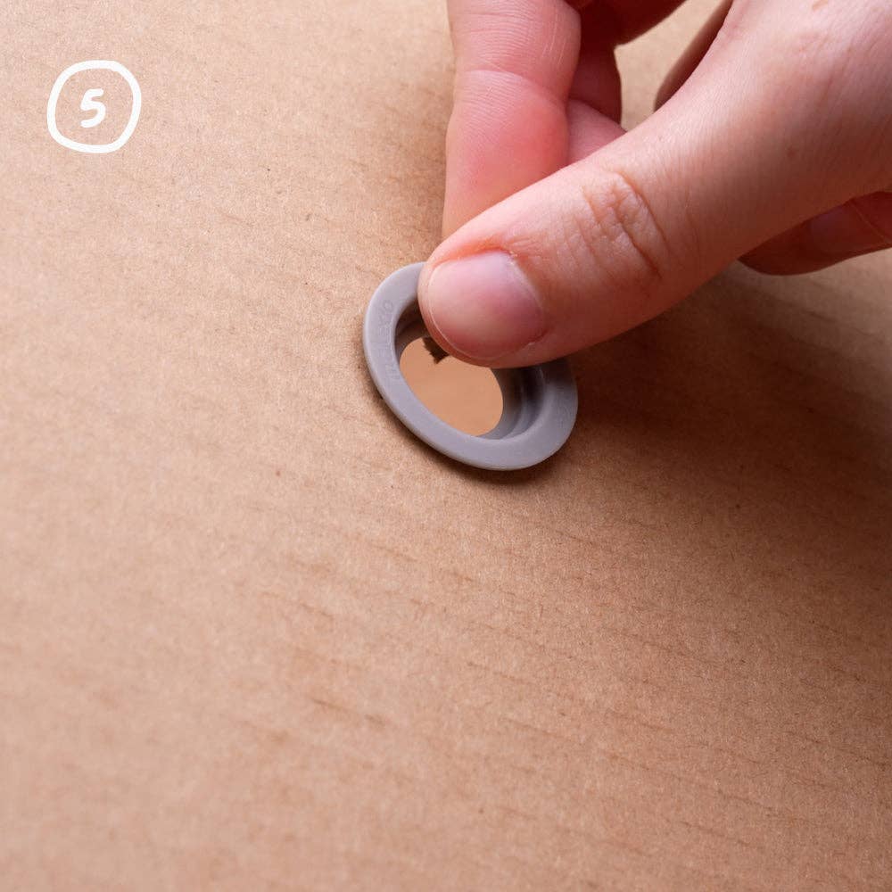 Hand legt einen grauen Makedo Roto-Ring auf das Loch im Karton, Schritt 5