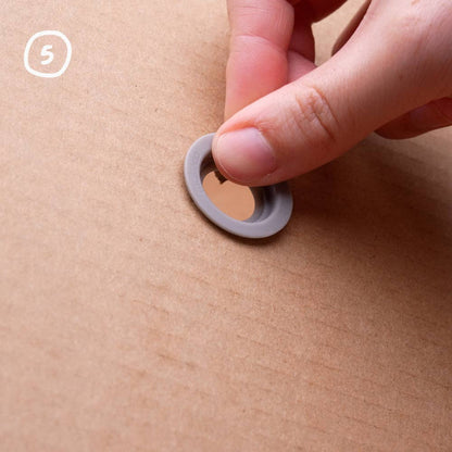 Hand legt einen grauen Makedo Roto-Ring auf das Loch im Karton, Schritt 5