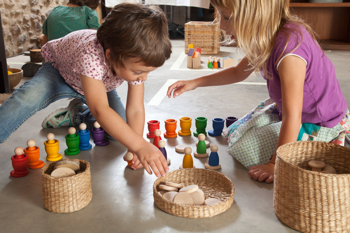 Zwei Kinder spielen mit Grapat Nins, bunten Holzfiguren in geflochtenen Körben sortiert