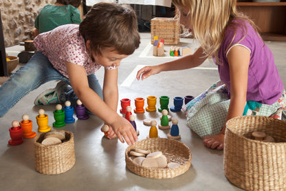 Zwei Kinder spielen mit Grapat Nins, bunten Holzfiguren in geflochtenen Körben sortiert