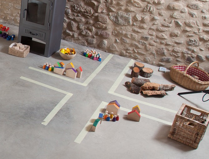 Grapat Houses and Nins auf Spielfläche arrangiert mit Holzhäusern, bunten Holzfiguren, Naturmaterialien und Körben in Szene