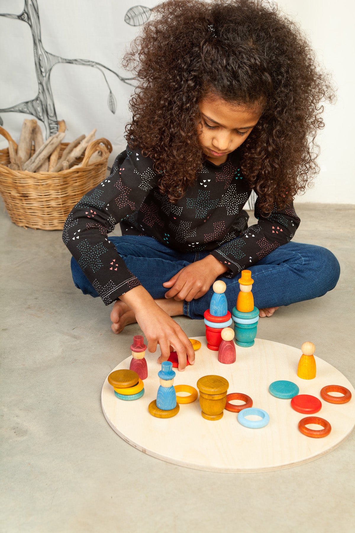 Kind spielt mit Grapat Aguamarina Summer, bunten Holzringen und Stöckchen auf weißer Spielplatte