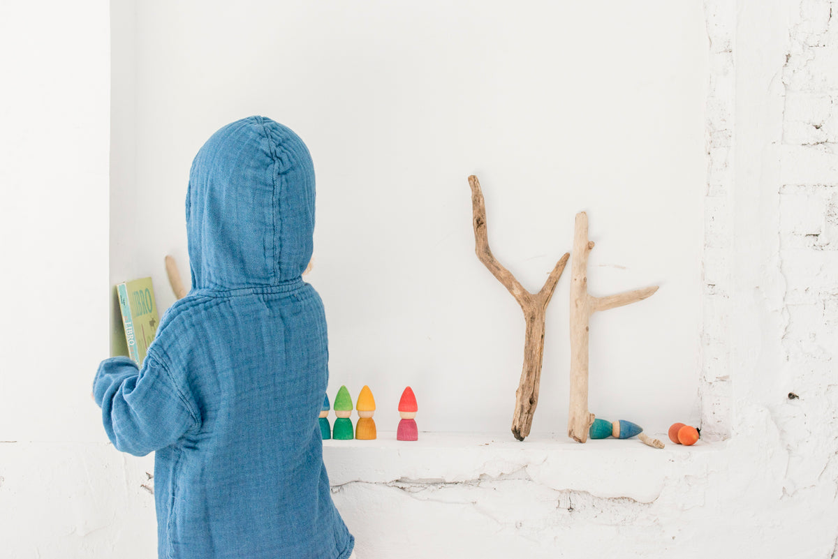 Kind von hinten in blauem Hemd spielt mit Grapat Rainbow Tomtens neben Ästen und Naturmaterialien