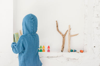 Kind von hinten in blauem Hemd spielt mit Grapat Rainbow Tomtens neben Ästen und Naturmaterialien