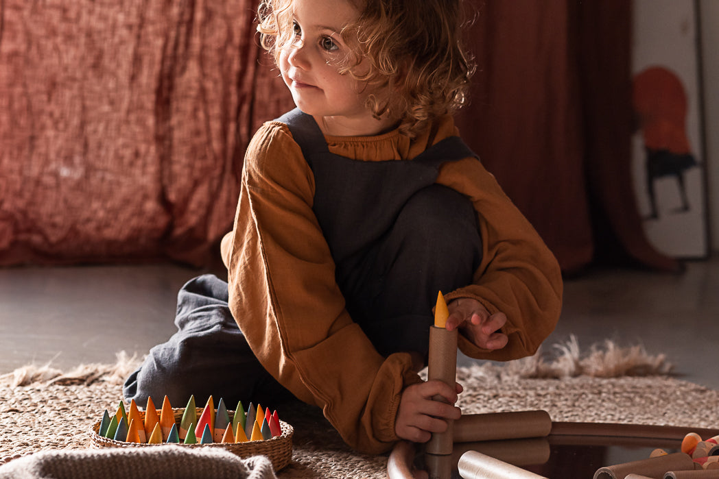 Kind mit lockigem Haar spielt sitzend mit Grapat Baby Sticks auf Teppich, hält einen orangen Stab in der Hand