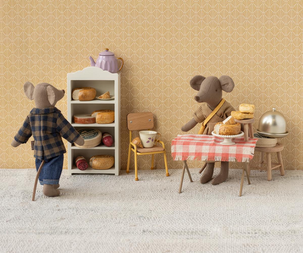 Maileg Papa Maus von hinten vor einem Regal mit Käse und Brot, daneben eine Maus am gedeckten Tisch