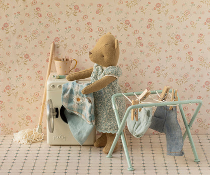 Teddy im Blümchenkleid hängt Wäsche auf den mintgrünen Maileg Wäscheständer neben der Waschmaschine