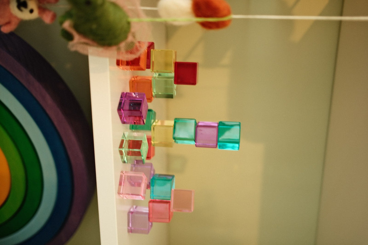 Bauspiel Lichtbauwürfel Pastell, transparente Würfel in Rosa, Rot, Orange, Grün und Türkis an Schnüren aufgehängt
