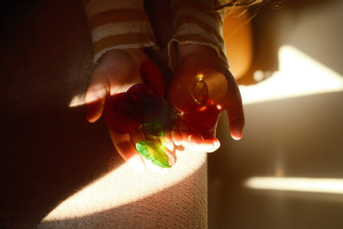 Kinderhände halten rote und grüne Bauspiel Funkelsteine transparent gegen Sonnenlicht, die Farben leuchten auf der Haut