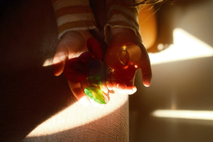 Kinderhände halten rote und grüne Bauspiel Funkelsteine transparent gegen Sonnenlicht, die Farben leuchten auf der Haut