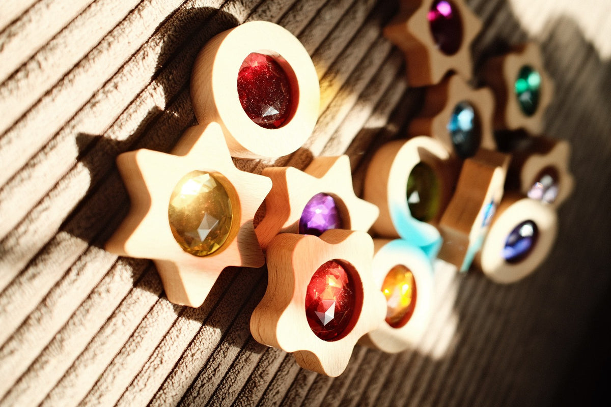 Bauspiel Spieltaler mit Funkelsteinen auf Holzuntergrund, Detailaufnahme mit roten, goldenen und violetten Steinen