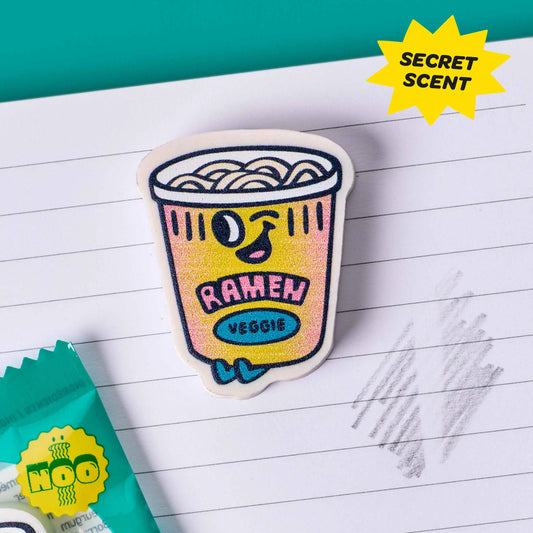 OMY Eraser Buddies Noo Radierer als gelber Ramen-Becher mit Nudeln, auf Notizpapier liegend