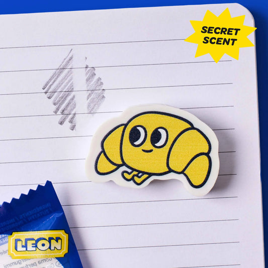 OMY Eraser Buddies Leon, gelber Croissant-Radierer mit Gesicht auf liniertem Notizpapier