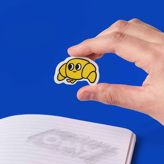 Hand hält den Croissant-Radierer OMY Eraser Buddies Leon vor blauem Hintergrund