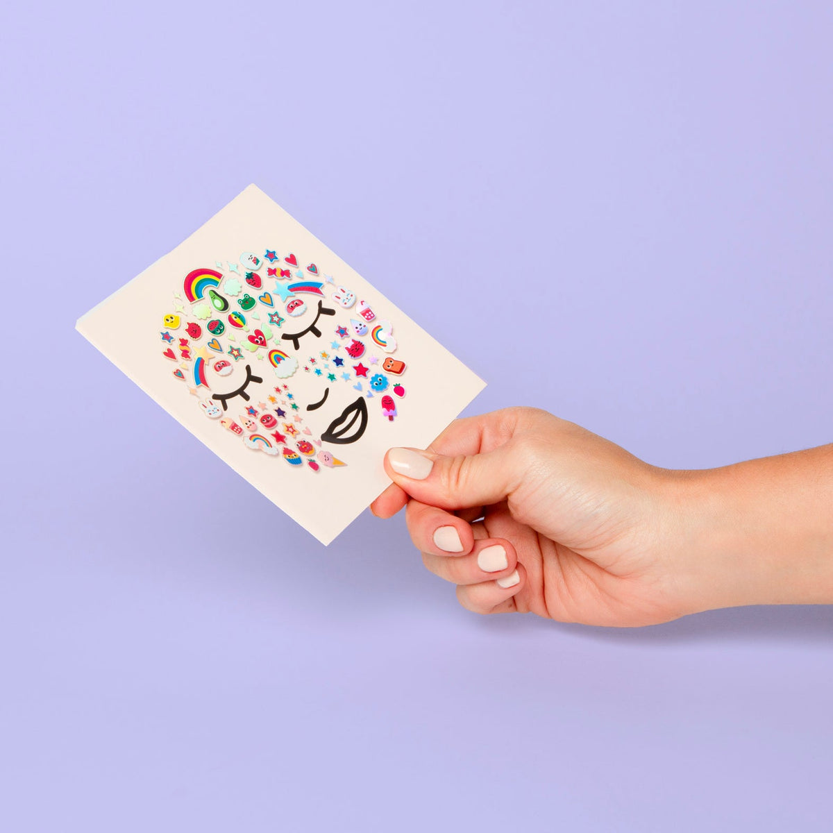 OMY Gesichtssticker Kawaii, Stickerbogen mit bunten Kawaii-Motiven in Hand vor lila Hintergrund