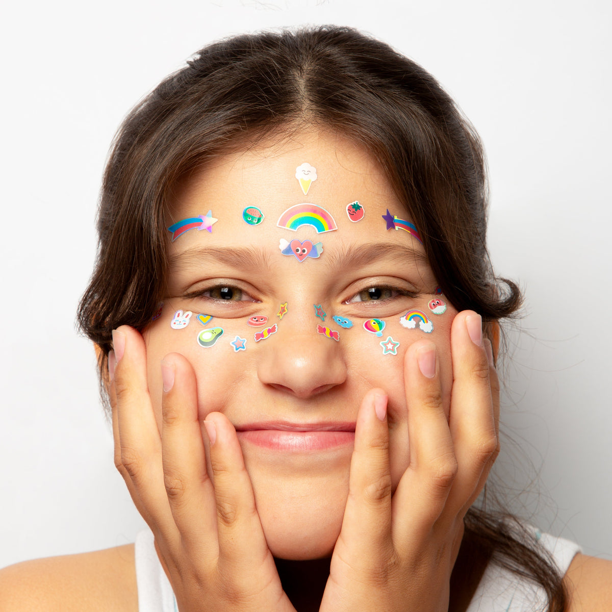 Mädchen trägt OMY Gesichtssticker Kawaii mit bunten Glitzer-Motiven auf Stirn und Wangen, hält Gesicht mit Händen