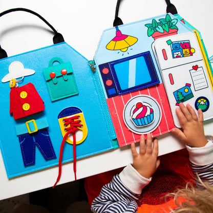 Kind mit OMY Montessori-Spielset, bunte Stoffseiten mit Knöpfen, Taschen und Schnüren in Blau und Rot