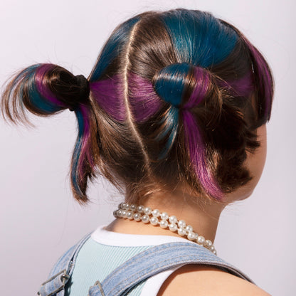 Kind von hinten mit zwei Zöpfen, Haare mehrfarbig mit OMY Haarkreide in Blau, Violett und Braun gefärbt, trägt Perlenkette