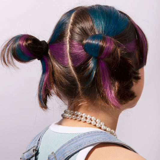 Kind von hinten mit zwei Zöpfen, Haare mehrfarbig mit OMY Haarkreide in Blau, Violett und Braun gefärbt, trägt Perlenkette