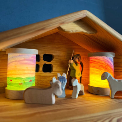 Zwei Toverlux Laternen mit selbst bemalten Schirmen leuchten in einem Holzstall mit Hirtenfigur und Holztieren